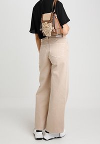 Beige wide-leg trousers with a high waist, worn with a black top, and a multi-colored backpack featuring a textured pattern. White sneakers.