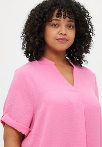 Rosa topp med en avslappet passform, korte rullede ermer og v-hals design. Laget av teksturert stoff, som fremhever et glatt utseende.