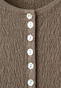Tissu tricoté brun texturé avec six boutons blancs alignés verticalement, alternant formes rondes et forme de fleur.