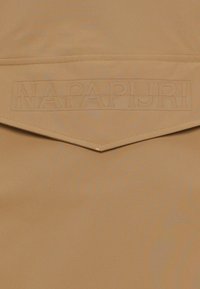 Υφασμα καμηλό με λεία υφή που διαθέτει ένα εξέχον ανάγλυφο λογότυπο "NAPAPIURI" στο κέντρο, τοποθετημένο πάνω σε ένα διακριτικό τονικό μοτίβο.