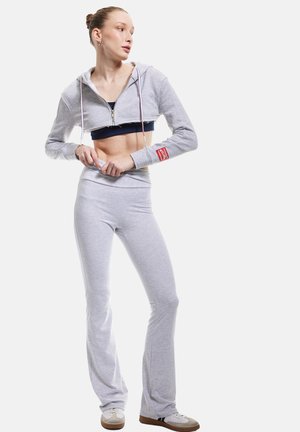 Haut à capuche gris court avec fermeture éclair, pantalon évasé gris assorti et baskets blanches. Comprend un top court bleu marine et un détail d'étiquette rouge sur les manches.