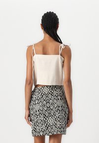 Kuttet beige linne topp med justerbare knytestroppar og et miniskjørt i svart og hvitt med geometriske mønster.