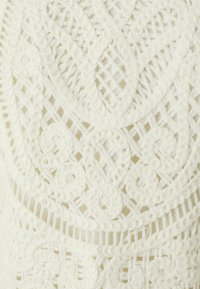 Tessuto di maglia bianco con un intricato motivo di pizzo caratterizzato da disegni vorticosi e sezioni a tessitura aperta, che conferiscono texture e profondità.