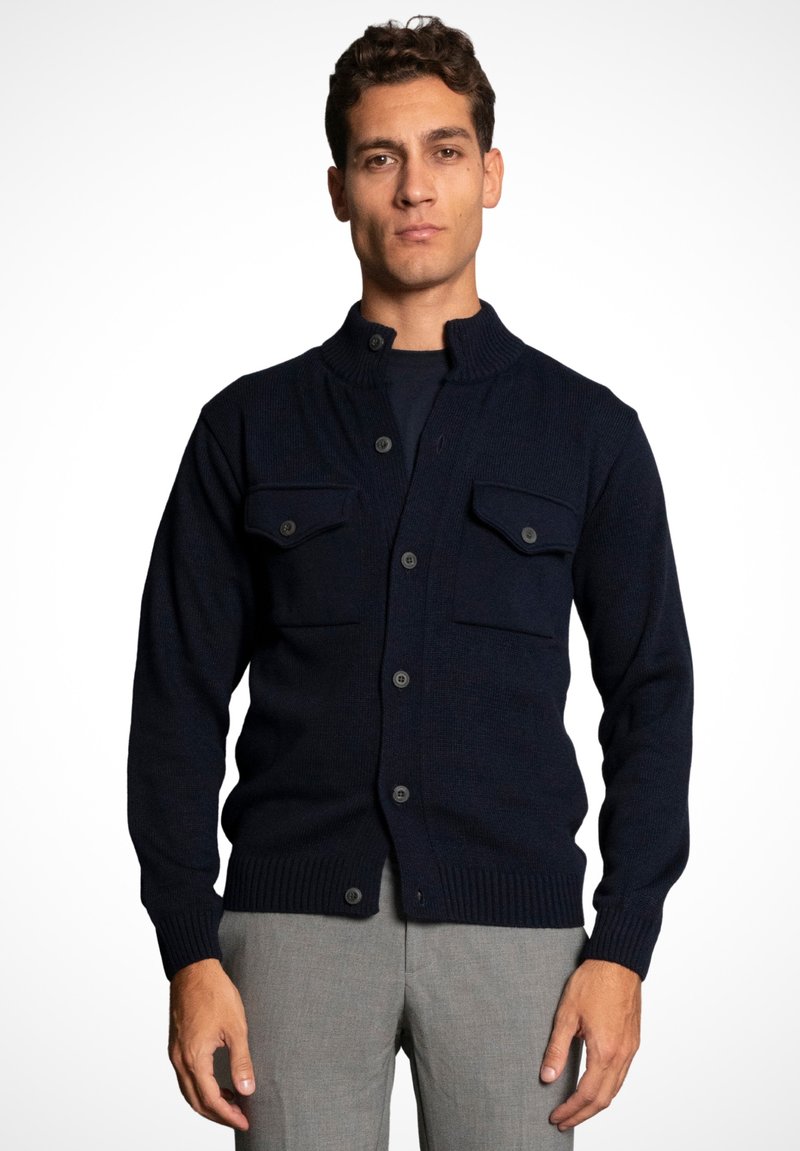Navy knitted cardigan with a high collar, featuring two front pockets and button closure. Ribbed cuffs and hemline. Simple and functional design.