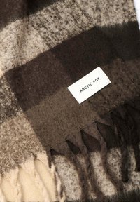 Bruine en beige geruite sjaal gemaakt van zacht materiaal, met franjes aan de randen en een wit label met de tekst "ARCTIC FOX."