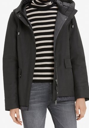 Sort vinterjakke med hætte, lynlås foran og sidelommer, båret over en sort-hvid stribet rullekrave og grå jeans.