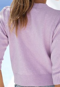 Young woman with long light brown hair wears a light purple knit sweater with puffed sleeves and ribbed hem, shown from behind.