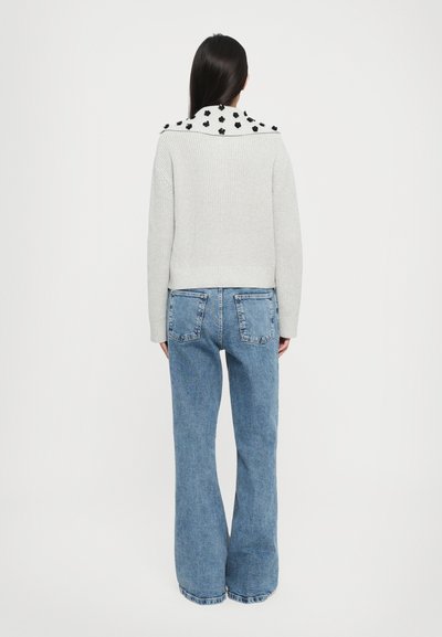 Pull en tricot gris avec un col à pois noirs, associé à un jean clair à taille haute et évasé, vu de dos.