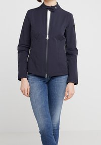 Navy blue jacket with a high collar, zip closure, and long sleeves. Smooth fabric with a fitted design and minimalistic style.