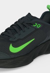 Μαύρο παπούτσι τρεξίματος Nike με φωτεινό πράσινο λογότυπο Swoosh και πράσινες τρύπες για κορδόνια σε υφή σόλας και επάνω μέρος.