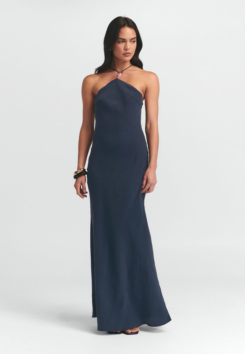 Navyblaues, bodenlanges Kleid mit Halterneck-Design, das mit einem Perlendetail am Ausschnitt sowie einem Seitenschlitz für mehr Bewegung versehen ist.