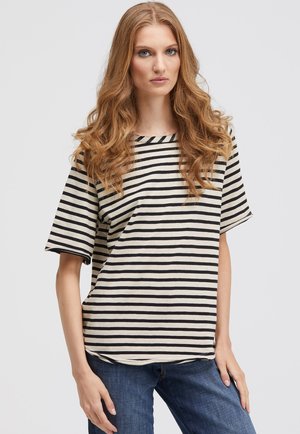 Striped top in cream and black, short sleeves, crew neck, relaxed fit, textured fabric. Worn with blue denim jeans.