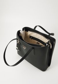 Sac en cuir noir avec une texture lisse, un intérieur spacieux, une doublure claire, des accessoires en or, et un accent de logo à l'avant.