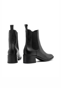 Czarne skórzane botki na kostkę z elastycznymi bokami, okrągłym noskiem i niskim, wyprofilowanym obcasem. Gładka tekstura z delikatnym połyskiem. Stylowo zaprojektowane uchwyty.