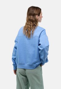 Sweatshirt bleu clair avec une coupe décontractée, col rond et manches à bords côtelés, associé à un pantalon rayé vert et blanc.