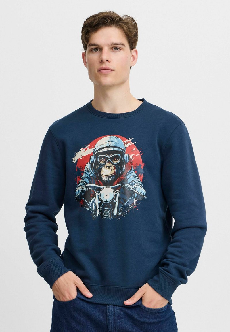 Sudadera de navy hecha de algodón con puños acanalados. Presenta un gráfico de un mono con un casco montando una motocicleta sobre un fondo rojo y blanco.