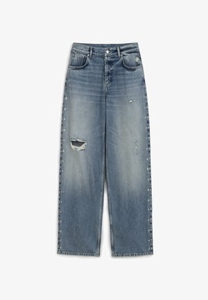 Jasnoniebieskie dżinsowe spodnie szerokie z postrzępieniami, widocznymi przetarciami oraz srebrnymi ćwiekami wzdłuż bocznych szwów. Klasyczny krój pięciu kieszeni.