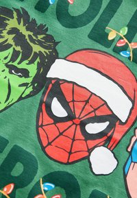 Zöld póló, amelyen Marvel karakterek szerepelnek, köztük Pókember karácsonyi sapkában és Hulk. Grafikai tervezés élénk színekkel és ünnepi díszítéssel.