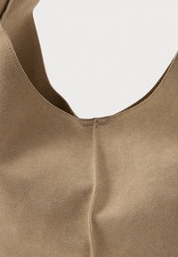 Borsa in suede color crema con una texture liscia, dotata di un'ampia apertura curva e cuciture minime. Linee pulite e design semplice.