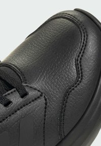 Scarpa sportiva nera in pelle con superficie texturizzata, forma arrotondata, cuciture a contrasto e lacci neri, con una suola in gomma liscia.