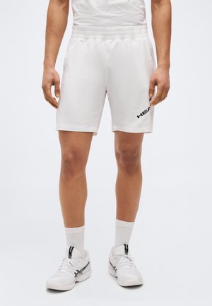 Fehér atléta rövidnadrágot viselő férfi fekete "HEAD" logóval, fehér sportzokniban és fehér Asics sportcipőben, egyszerű fehér háttér előtt áll.