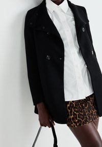 Černý dvouřadý kab�át s velkými knoflíky, bílá košile s límečkem pod ním a mini sukně s leopardím potiskem. Texturovaná tkanina s viditelnými švy.