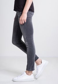 Szare wąskie dżinsy wykonane z denimu, charakteryzujące się dopasowanym krojem, lekkim wyblaknięciem i klasycznym pięciopunktowym stylem, w połączeniu z białymi trampkami.