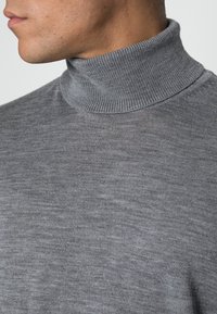 Pull à col roulé gris avec texture côtelée et col. Vue en gros plan mettant en valeur le détail du tricot et la qualité du tissu doux.