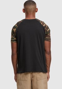 Black crew neck t-shirt with camo short sleeves, cotton material, fitted design, and a straight hem. Back view showing sleeve pattern detail.