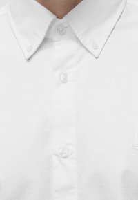 Gros plan d'une personne portant une chemise blanche boutonnée avec un col boutonné.