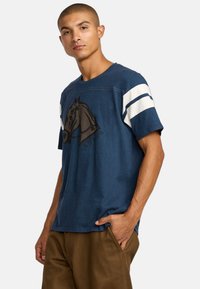 T-shirt à manches courtes bleu marine avec un graphique de cheval, des manches rayées blanches et bleues, et une coupe décontractée. Texture de tissu douce.