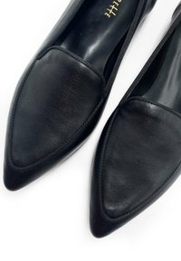 Bailarinas de cuero negro con un diseño de punta afilada, que cuentan con una textura suave y un sutil cosido alrededor de los bordes para detalle.