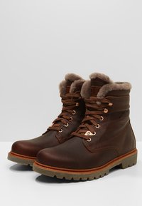 Botas de cuero marrón con forro de piel, diseño de cordones, exterior texturizado y suela de goma con un patrón de tracción robusto.