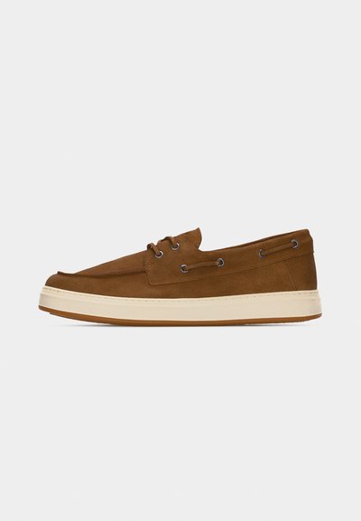Chaussure bateau décontractée en daim marron avec semelle en caoutchouc crème, détails lacets sur les côtés et deux œillets à l'avant, vue de profil latéral.