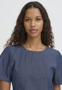 Robe en denim à manches courtes, col rond et coutures apparentes. Le tissu a une finition texturée dans une teinte bleu foncé.