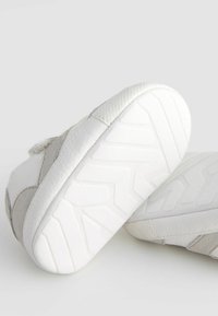Chaussures grises et blanches avec un dessus texturé, présentant un design rayé et une semelle en caoutchouc avec un motif en zigzag pour une meilleure adhérence.