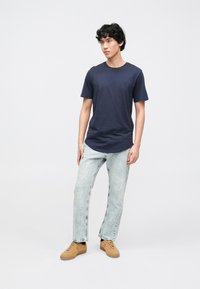 Camiseta de manga corta azul marino con cuello redondo, combinada con vaqueros de lavado claro y zapatillas marrón claro. Textura suave, ajuste casual.