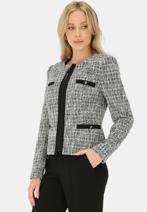 Szara tweedowa marynarka z czarnymi akcentami, zapinana na zamek, z dwoma kieszeniami na piersi i teksturowaną tkaniną. Dopasowany krój i długie rękawy.