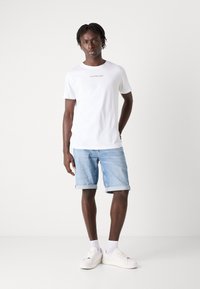 Fehér pamut póló "Calvin Klein Jeans" logóval, világoskék farmer rövidnadrággal és fehér sportcipővel párosítva. Egyszerű, laza dizájn.