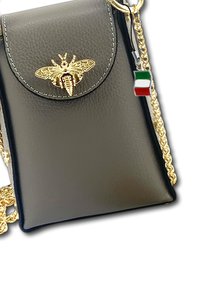 Zwarte leren schoudertas met een gouden bijembleem, gouden kettingriem en een klein Italiaans vlaggetje eraan bevestigd. Gladde textuur, rechthoekige vorm.