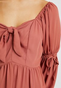 Hedvábná růžová blůza se čtvercovým výstřihem, detailem mašle a elastickými balónovými rukávy. Lehce splývavá tkanina s jemnou strukturou.