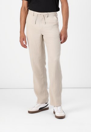 Lys beige linbukser med en avslappet passform, med elastisk midje og snor. Matchet med hvite sneakers.