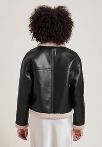 Czarna skórzana kurtka z ociepleniem z owczej wełny, krótki fason i długie rękawy. Charakteryzuje się wyraźnym poziomym szwem na plecach.