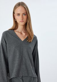 Grijze langesleeve top met een V-hals, gemaakt van zachte stof. Heeft een ontspannen pasvorm en minimale naden voor een eenvoudig, functioneel ontwerp.