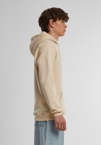 Creme hoodie med snoretræk i hætten, ribbede manchetter og en kengurulomme, lavet af blødt, struktureret stof. Båret med lyse denimbukser.