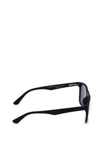 Lunettes de soleil polarisées noires avec une monture enveloppante posées à plat montrant le côté intérieur des branches et des verres.