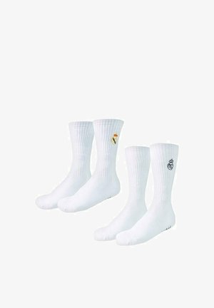 Dwie pary białych skarpet sportowych z haftowanym logo klubu piłkarskiego Real Madrid u góry.