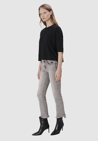 Czarny, krótki t-shirt z krótkim rękawem w zestawie z jasnoszarymi, zniszczonymi skinny jeansami. Stylizacja uzupełniona o czarne, szpiczaste botki za kostkę.