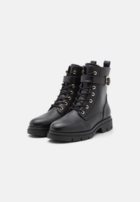 Bottes ankle en cuir noir avec un laçage à l'avant, œillets dorés, détail de sangle à boucle et semelle texturée robuste.