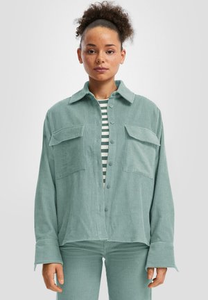 Lichtgroene corduroy shirtjas met een ontspannen pasvorm, voorzien van twee borstzakken, een puntige kraag en knoopsluiting. Gestreepte top eronder.